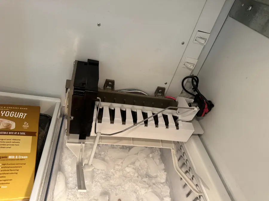 Ice maker mounted above an overfilled ice bin in a freezer
