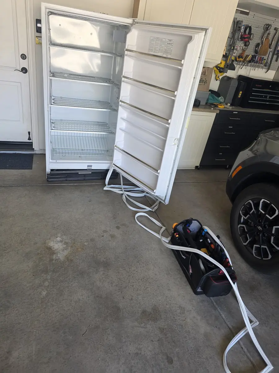 Upright freezer in a garage with the door open during a repair