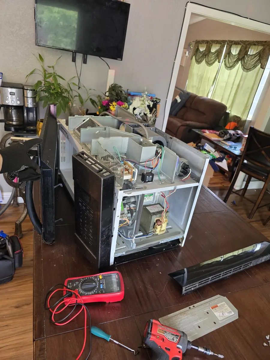 Microwave disassembled on a table with a multimeter for diagnosis